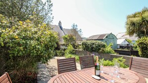 A wooden table with four chairs, a bottle of wine, and several glasses on a patio. - Firkin Cottage (Weymouth)