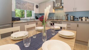 A modern kitchen with white cabinets, a dining table set for four, and a window with a view of greenery. - 40 Skiptory Howe (Windermere)