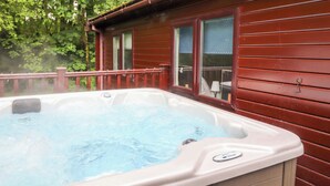 A hot tub outside a wooden cabin with a wooden deck and a window. - 40 Skiptory Howe (Windermere)