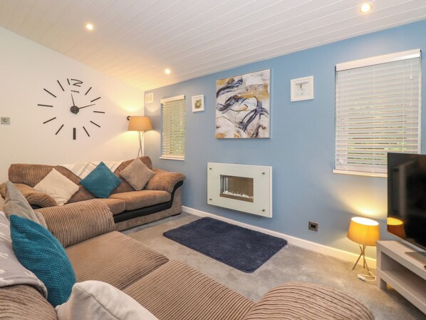 A living room with a sofa set, a wall clock, artwork, a fireplace, and a television. - 40 Skiptory Howe (Windermere)