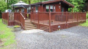 A cabin with a wooden deck, a covered porch, and a gravel driveway. - 40 Skiptory Howe (Windermere)