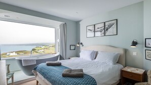 Une chambre à coucher avec un grand lit, une vue sur la mer, une baignoire et une petite table avec une lampe.