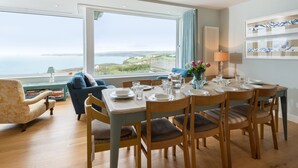 Un coin repas avec une table dressée pour six personnes, une vue sur la mer et un espace salon confortable avec un canapé et un fauteuil bleus.