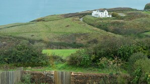 Une maison blanche avec un mur de pierre et une clôture en bois, située dans un espace verdoyant avec vue sur la mer.