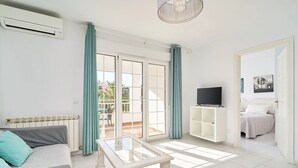 A modern living room with a sofa, a glass coffee table, a TV on a white cabinet, and a balcony with curtains. - Suite Nº 5 (1 double room and 1 single room) (Nerja)