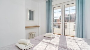 A hotel room with a large bed, a small bedside table, a mirror, and a view of the outside through a sliding glass door. - Suite Nº 5 (1 double room and 1 single room) (Nerja)