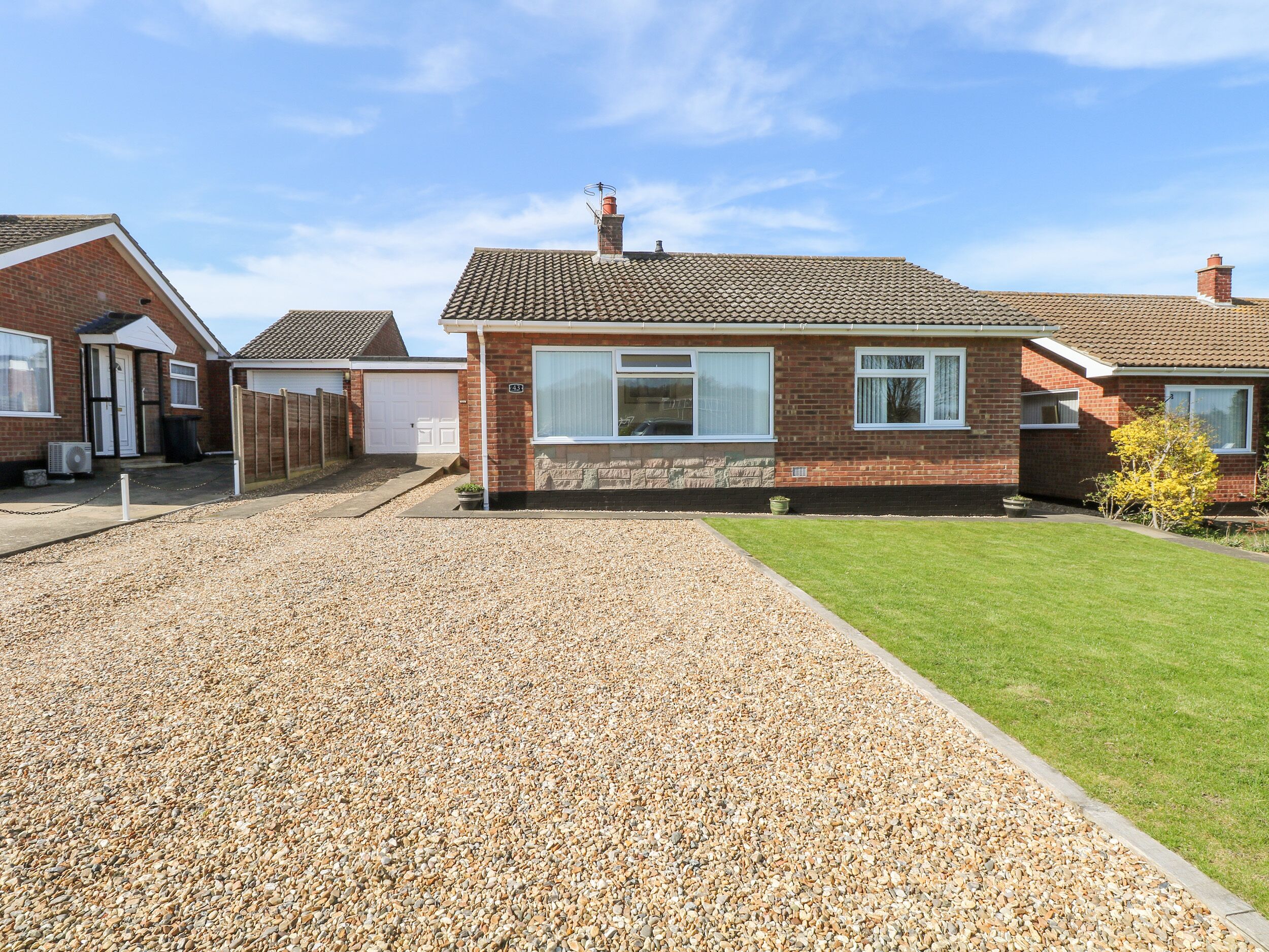 A residential property with a paved driveway, a grassy lawn, and a brick house with a tiled roof.