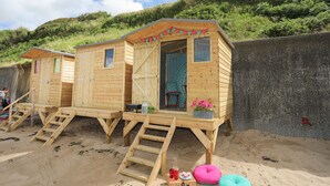 Bungalows de praia de madeira com escadas externas, uma mesa pequena e um candeeiro.