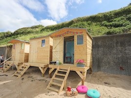 Cabañas de playa de madera con escaleras exteriores, una pequeña mesa y un farol.