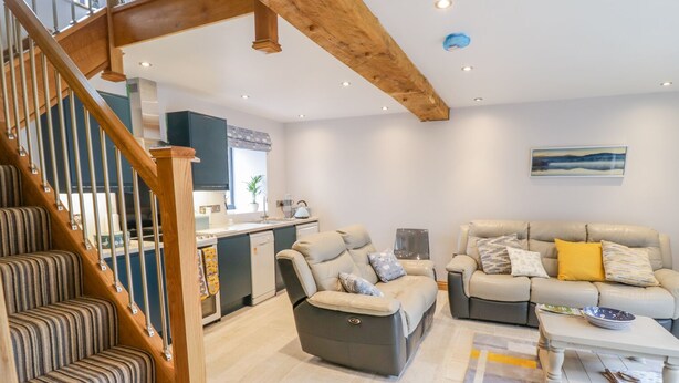 A modern living room with a staircase, two sofas, a coffee table, and a kitchen in the background. - 7evern @ Porth Farm (Caersws)