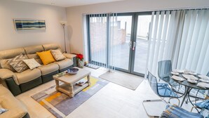 A modern living room with a sofa, coffee table, and dining area. - 7evern @ Porth Farm (Caersws)