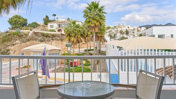 A balcony with a glass table and two chairs, overlooking a coastal town with white buildings and palm trees. - Suite Nº 9 (2 double rooms) (Nerja)