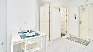 A small, clean room with a white table set for two, a white chair, and a door with a red sign. - Suite Nº 9 (2 double rooms) (Nerja)
