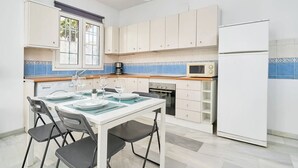 A compact kitchen with white cabinets, a white refrigerator, a microwave, and a dining table set for four. - BB Suite (3 double rooms) (Nerja)
