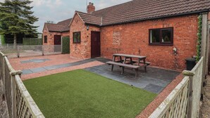 A brick house with a tiled roof, a wooden fence, and a grassy lawn.