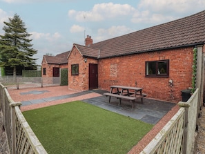 A brick house with a tiled roof, a wooden fence, and a grassy lawn.