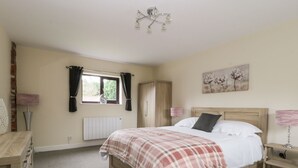 A bedroom with a bed, a wardrobe, a radiator, a window with curtains, a painting on the wall, and a bedside table with a lamp.