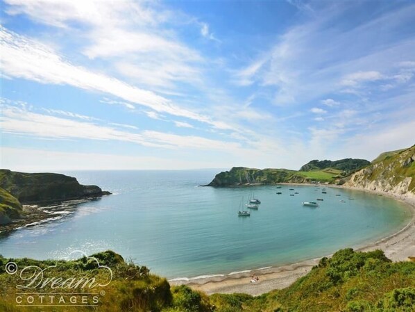 A coastal landscape with a beach, boats, and cliffs.