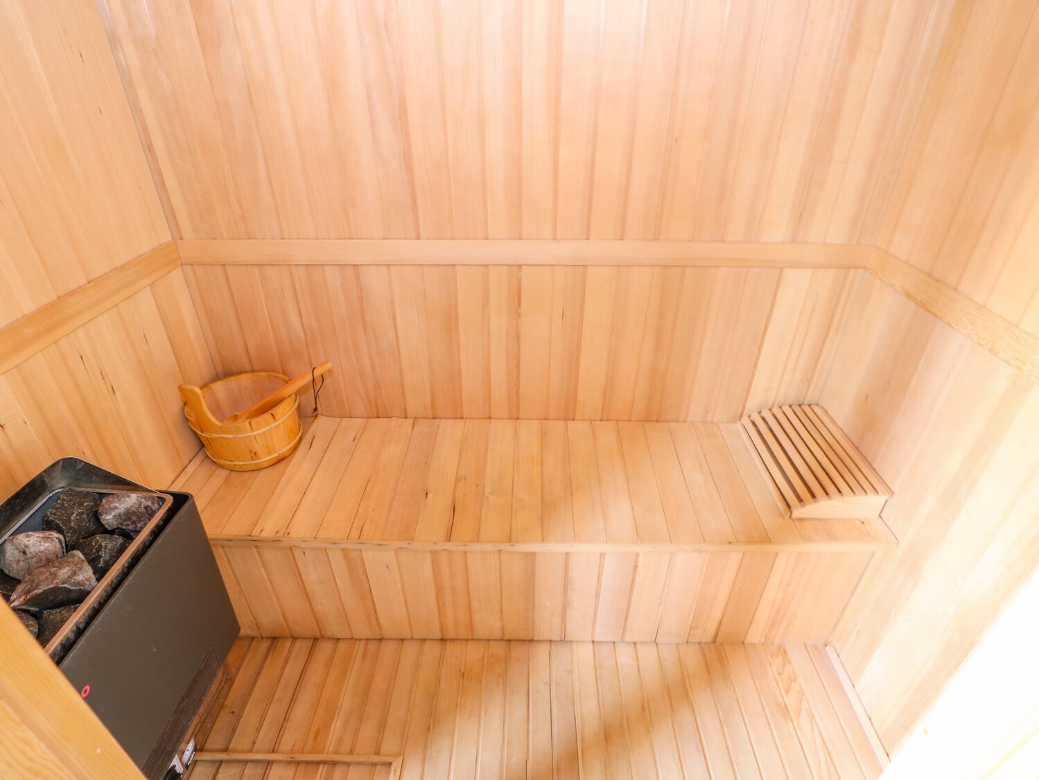 Un sauna en bois avec un banc, un seau et un appareil de chauffage.