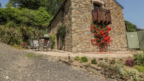 A stone building with a balcony, surrounded by a garden with various plants and flowers.