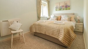 A bedroom with a bed, a chair, a nightstand, and a window with curtains.