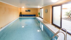 An indoor swimming pool with a blue tiled floor, a bench along one wall, and a door leading outside.