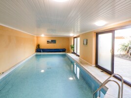 Una piscina interior con suelo de baldosas azules, un banco a lo largo de una pared y una puerta que da al exterior.