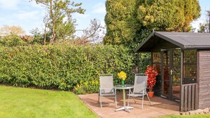 A patio with two chairs and a table, a small wooden structure, and a well-maintained hedge. - Stonecroft Lodge (Belper)