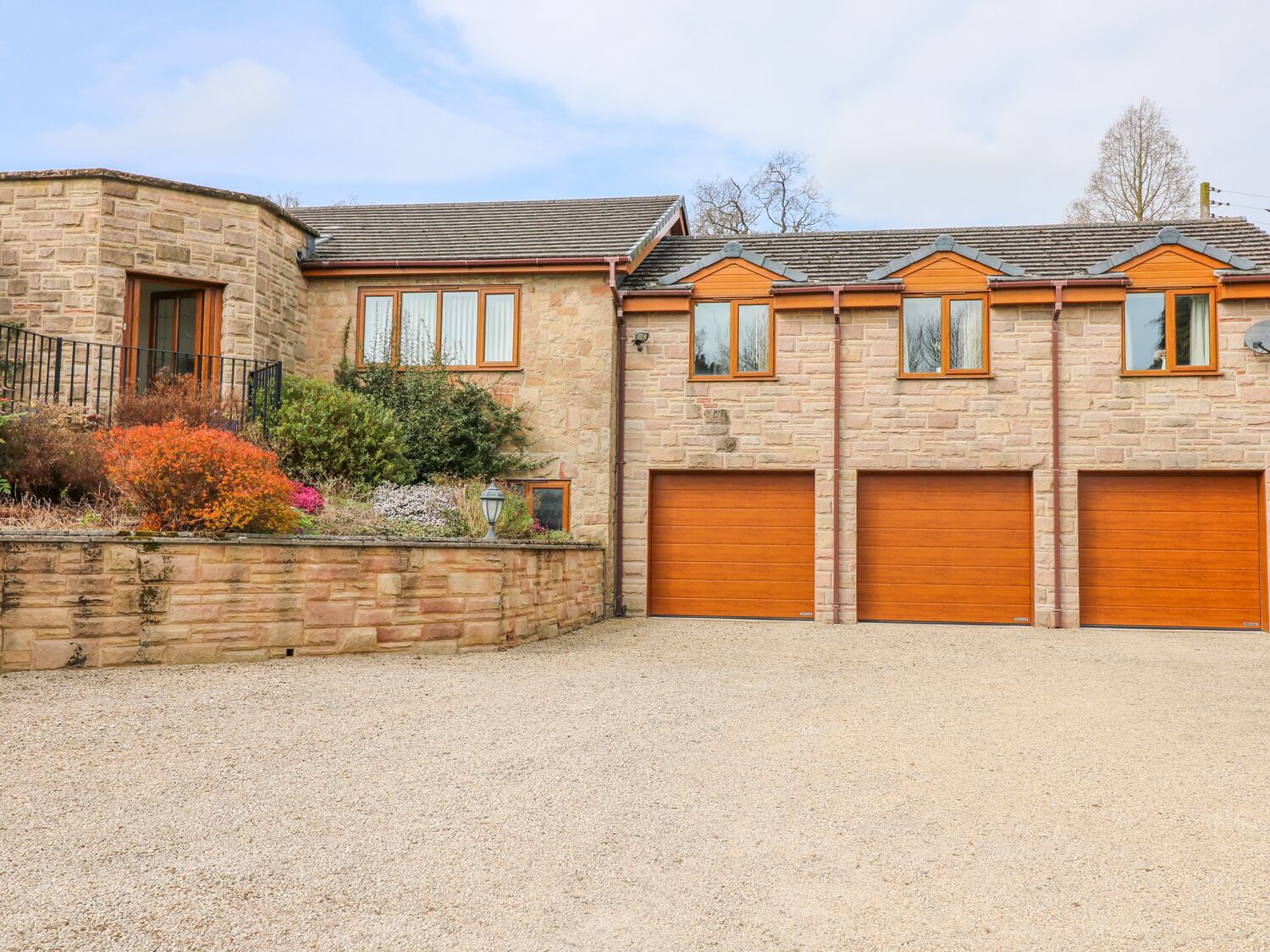 A two-story stone house with a gravel driveway and a landscaped garden.