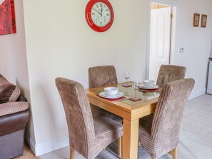 Un comedor con una mesa de madera, cuatro sillas acolchadas, un reloj de pared rojo y una puerta al fondo.