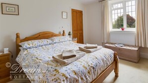 A bedroom with a wooden bed, a window with curtains, a bedside table, and a wall-mounted lamp. - Grazeland Cottage (Bridport)