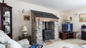 A cozy living room with a stone fireplace, a television, and comfortable seating. - Grazeland Cottage (Bridport)