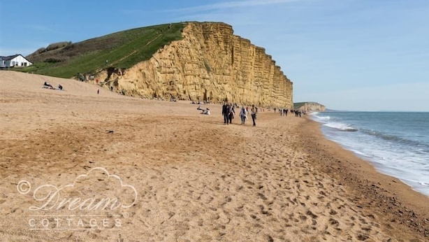 Ein Sandstrand mit einer großen Felsformation und einigen Spaziergängern.