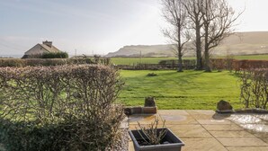 A patio area with a stone floor, potted plants, and a view of a rural landscape including a house and trees. - Orchard Cottage (Whitby)
