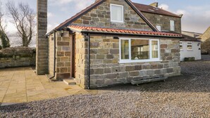 A stone cottage with a tiled roof, a chimney, and a gravel driveway. - Orchard Cottage (Whitby)