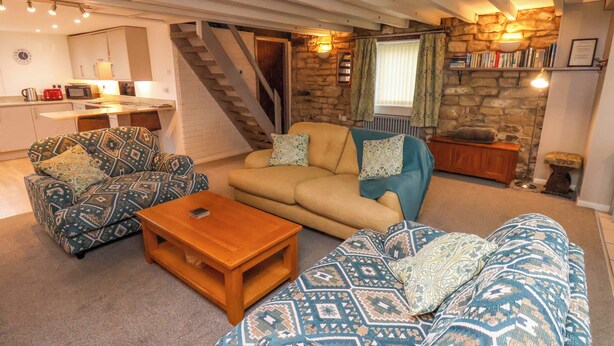 A cozy living room with a sofa, two armchairs, a coffee table, and a staircase leading to an upper level. - Orchard Cottage (Whitby)