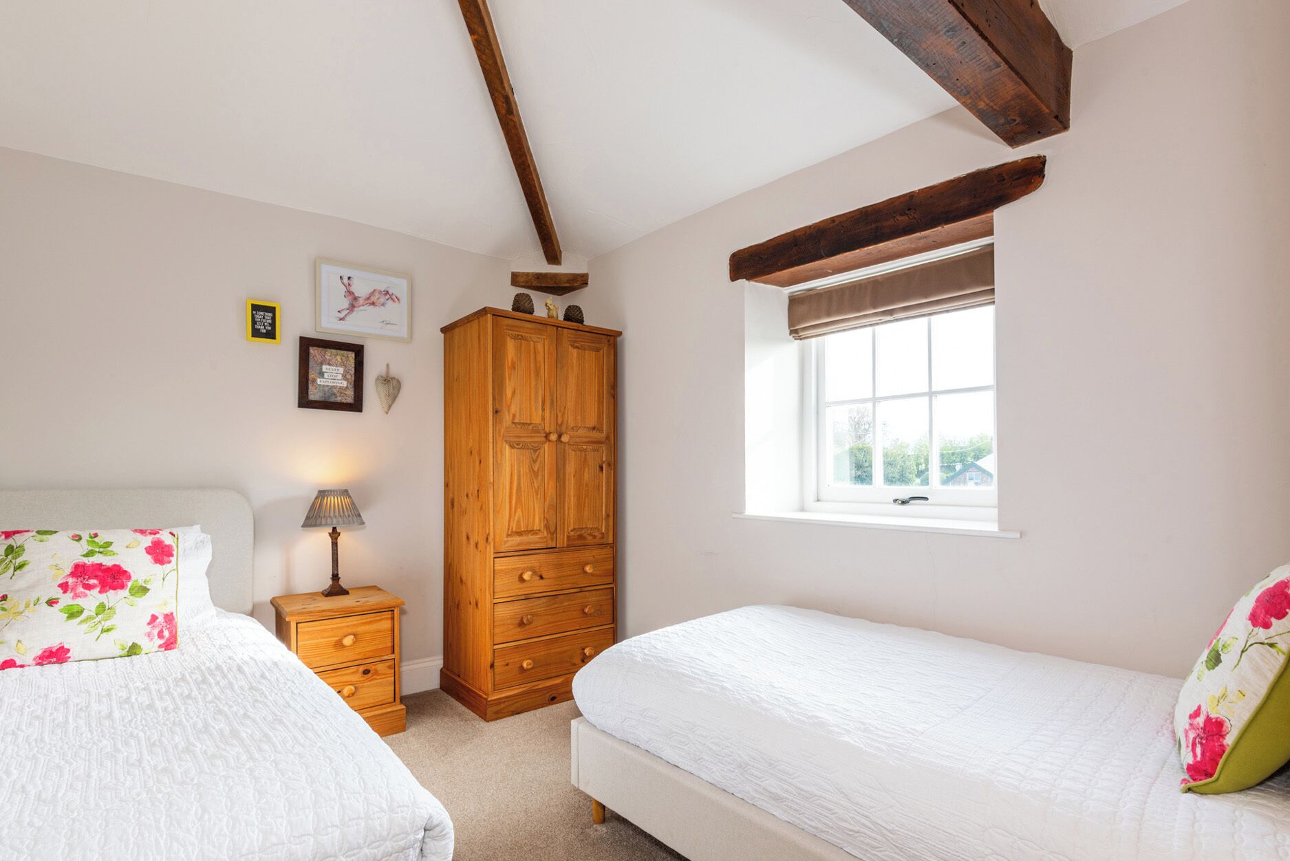 Une chambre avec deux lits, une armoire en bois, une table de chevet avec une lampe et une fenêtre donnant sur un beau paysage.