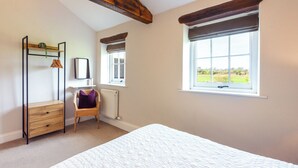 Ein Schlafzimmer mit Bett, Sessel, Schminktisch, Spiegel und zwei Fenstern mit Fensterläden.