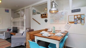 Un coin repas avec une table en bois dressée pour quatre personnes, des chaises bleues et un luminaire suspendu.