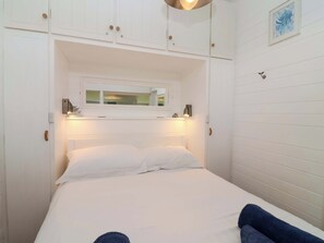 A bed with white linens, a headboard with a mirror, and two wall-mounted light fixtures.