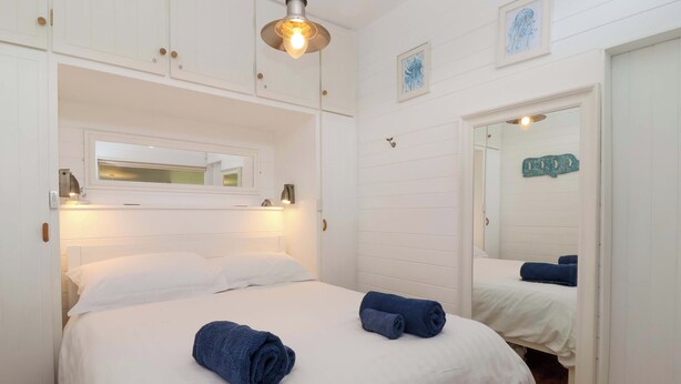 Une chambre à coucher avec un lit, deux serviettes enroulées, un miroir et un luminaire suspendu.