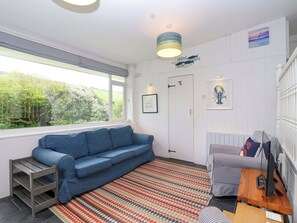 A room with a blue sofa, a striped armchair, a patterned rug, a wooden side table with a television, and a door with a fish decoration.