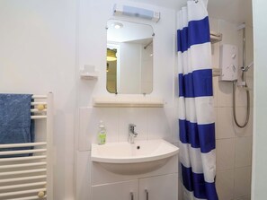 Um banheiro com pia branca, espelho, chuveiro com cortina azul e branca listrada e um porta-toalhas com toalha azul.