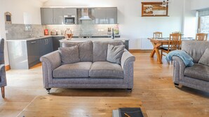 A spacious living area with a sofa, a dining table, and a kitchen in the background. - Apple Tree Cottage (Appleby-in-Westmorland)