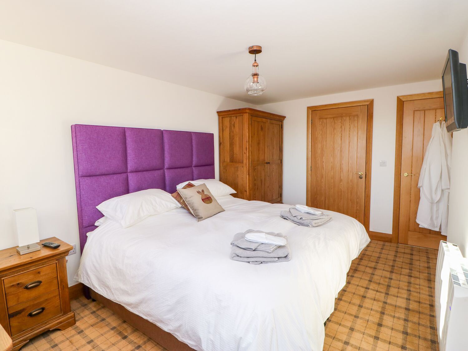A neatly made bed with white bedding, a purple headboard, and a wooden wardrobe.