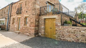 A stone building with a wooden door and a balcony with metal railings. - Apple Tree Cottage (Appleby-in-Westmorland)
