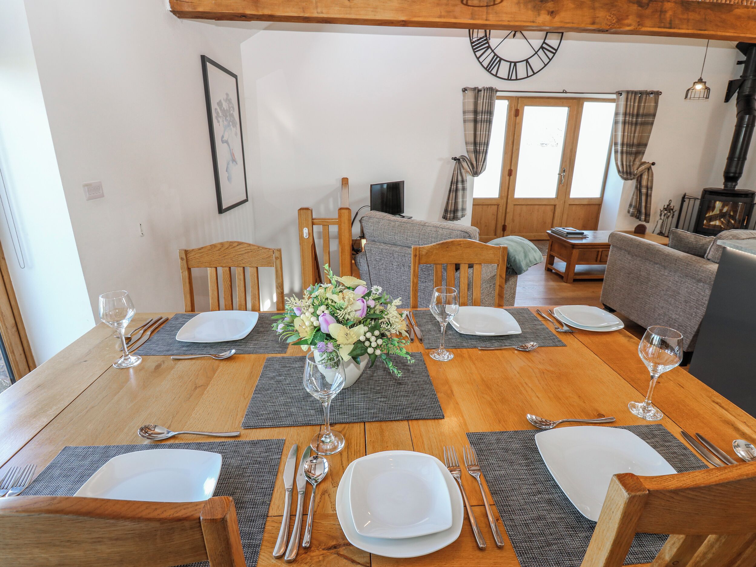 Un coin repas avec une table en bois dressée pour quatre personnes, entourée de chaises, avec un canapé et un téléviseur en arrière-plan.