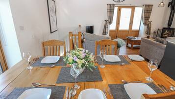 Un coin repas avec une table en bois dressée pour quatre personnes, entourée de chaises, avec un canapé et un téléviseur en arrière-plan.