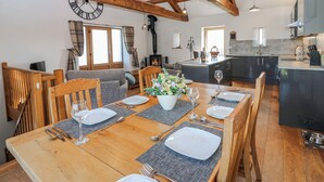 A dining area with a wooden table set for four, a sofa, and a kitchen in the background. - Apple Tree Cottage (Appleby-in-Westmorland)