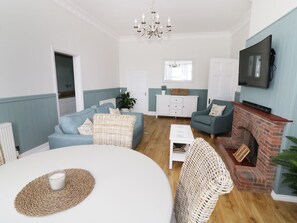 A living room with a blue sofa, a white coffee table, a wicker chair, a fireplace, and a television mounted on the wall.